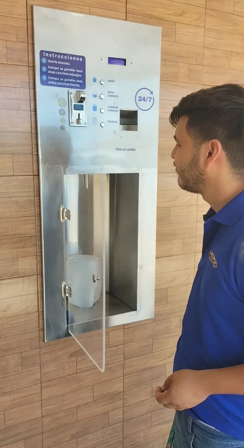Persona llenando un garrafón en dispensadora de agua automática empotrada en muro de azulejos (HIDROMAS)